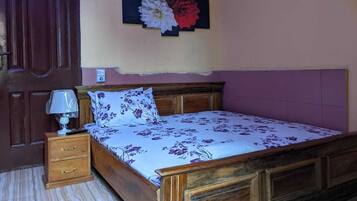 A bedroom with a wooden bed, a nightstand with a lamp, a door, and a wall-mounted artwork.