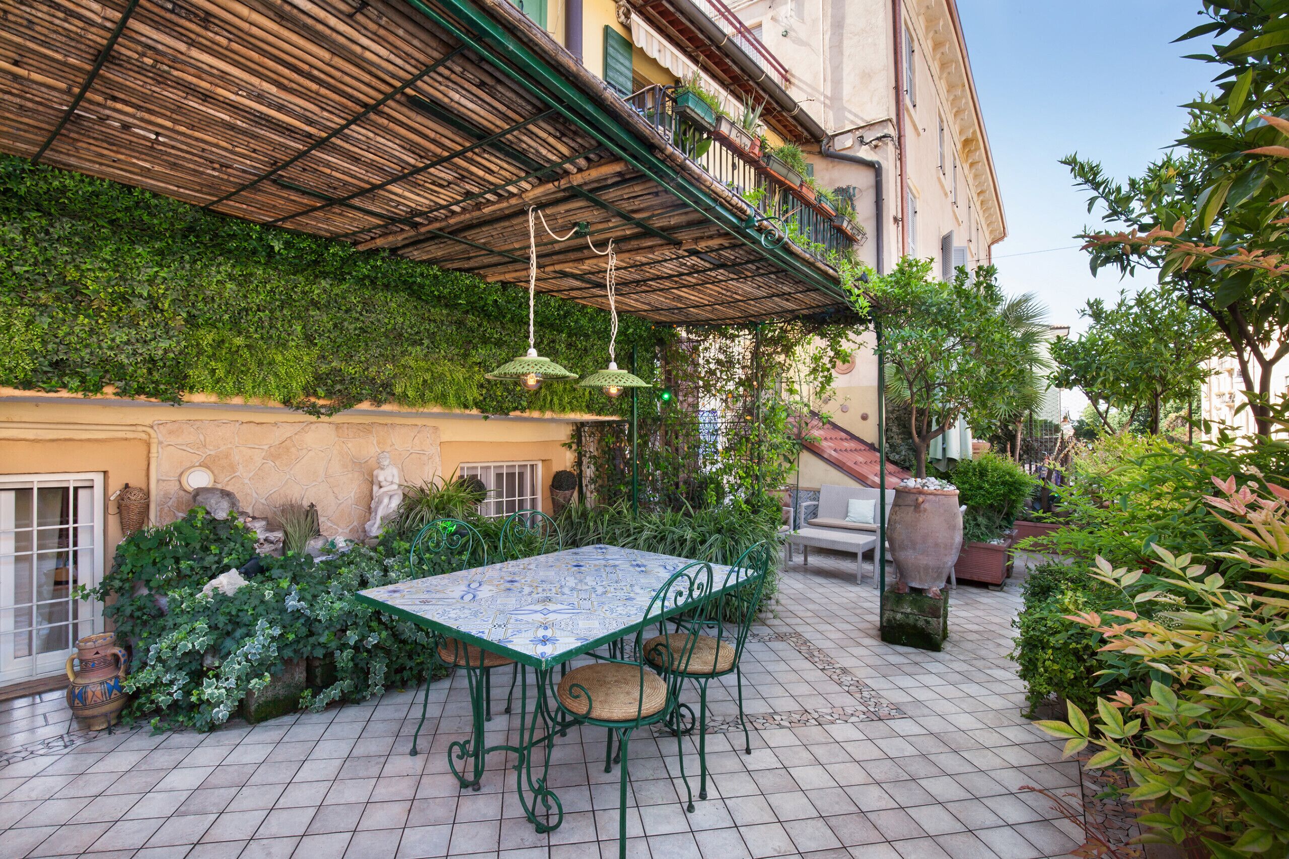 Een terras met een tafel en stoelen, omringd door groen en een betegelde vloer.