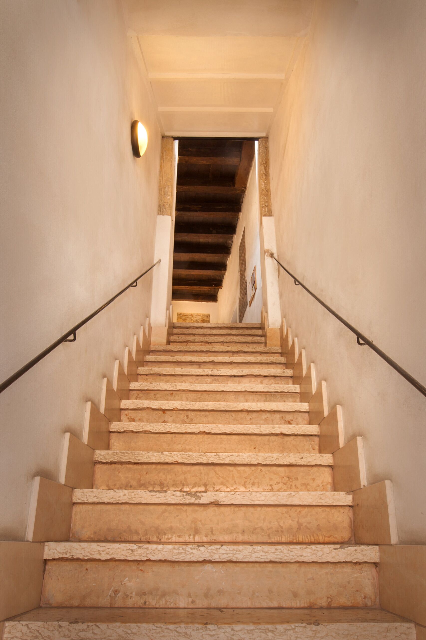 A staircase with a handrail on both sides, leading to a landing with a wooden ceiling.