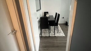 Un estrecho pasillo que conduce a un comedor con una mesa, sillas, una alfombra y un cuadro en la pared.