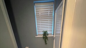 Una escalera estrecha con suelo de madera que da a una plataforma. Se ve una ventana con persianas en la pared de la plataforma, y una planta cuelga del alféizar.