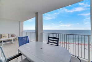 Un balcón con mesa y sillas blancas, un sofá, y vistas a la playa y al océano.