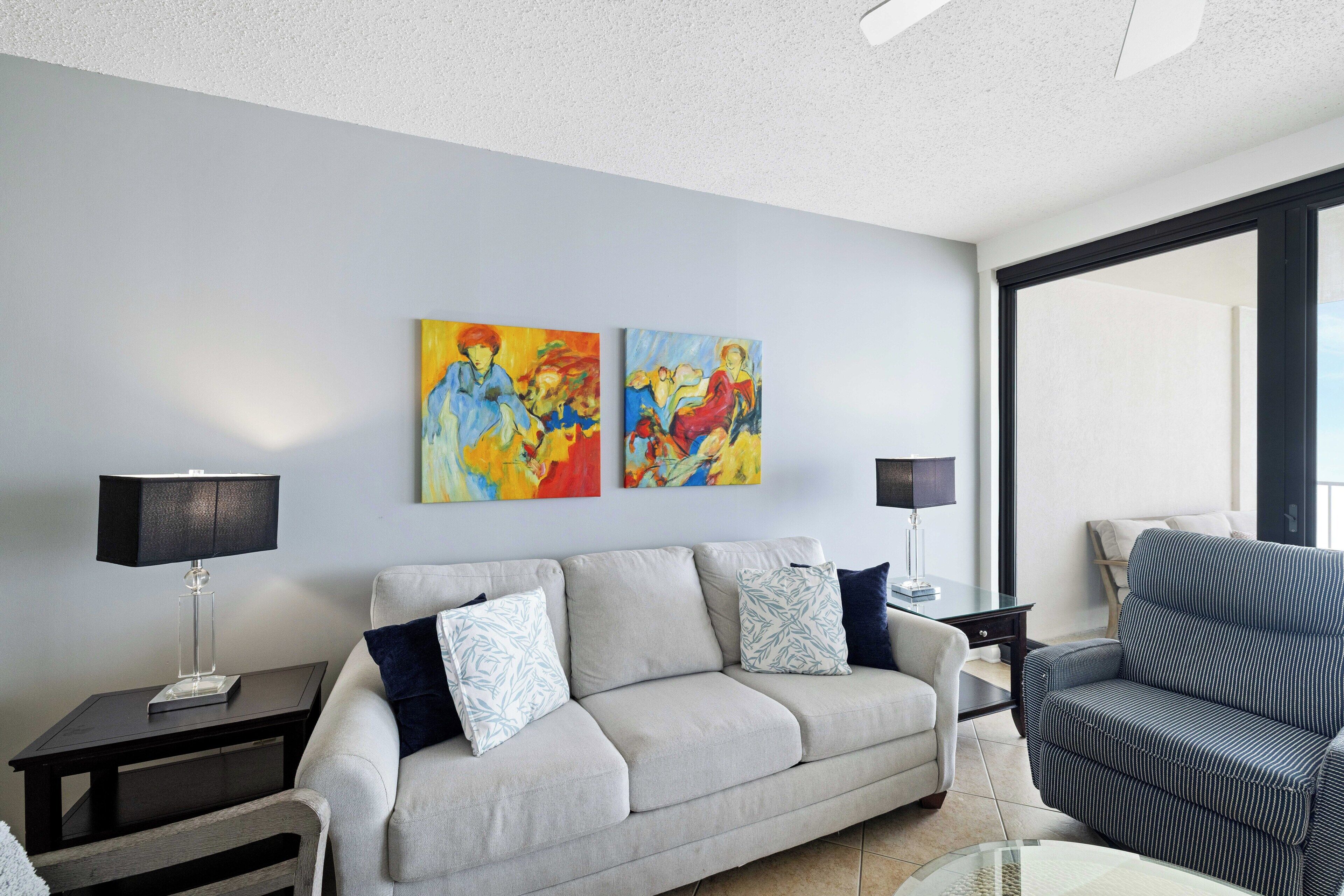 A living room with a sofa, a chair, two paintings on the wall, and a lamp on a side table.