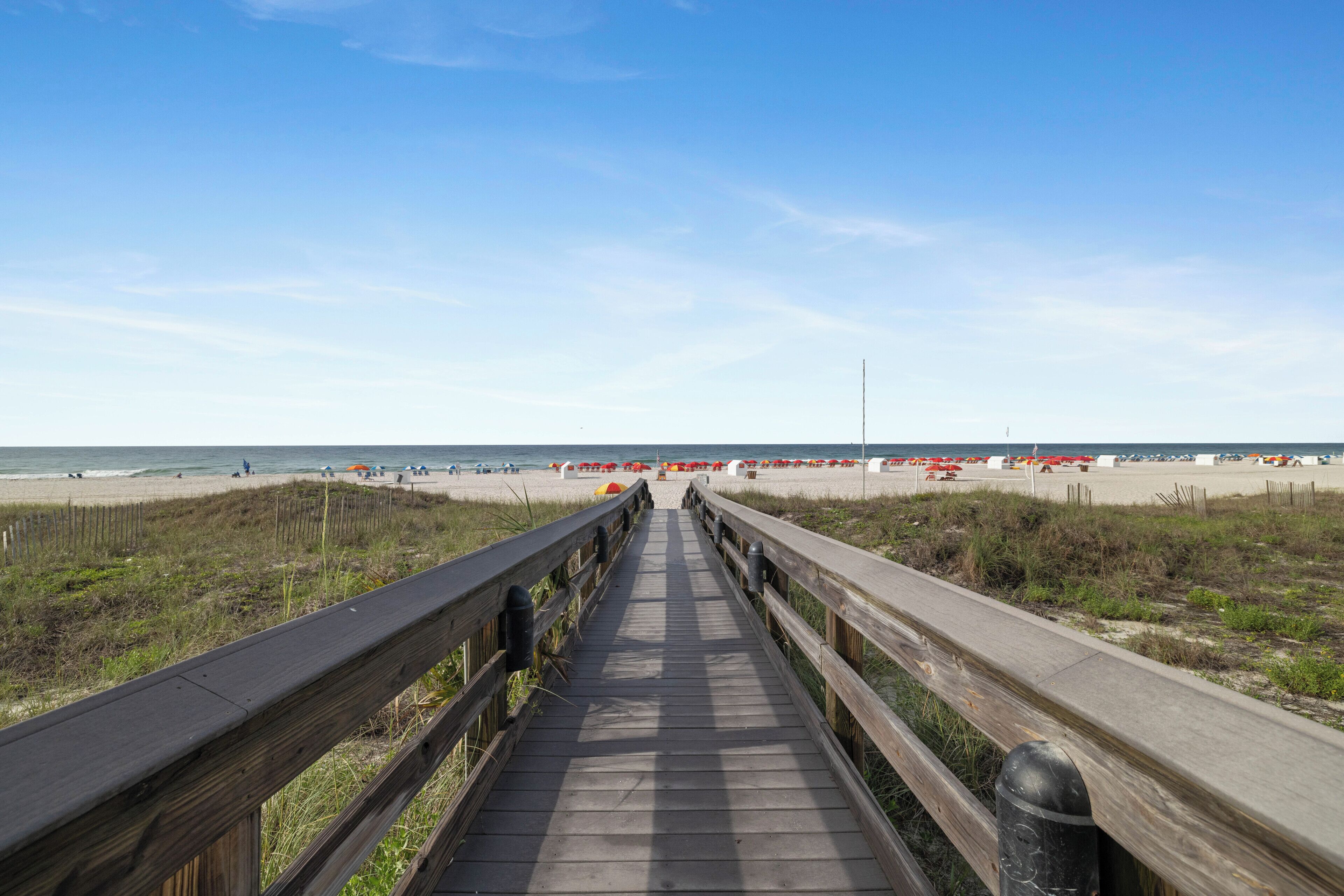 Een houten looppad naar een strand met parasols en ligstoelen.
