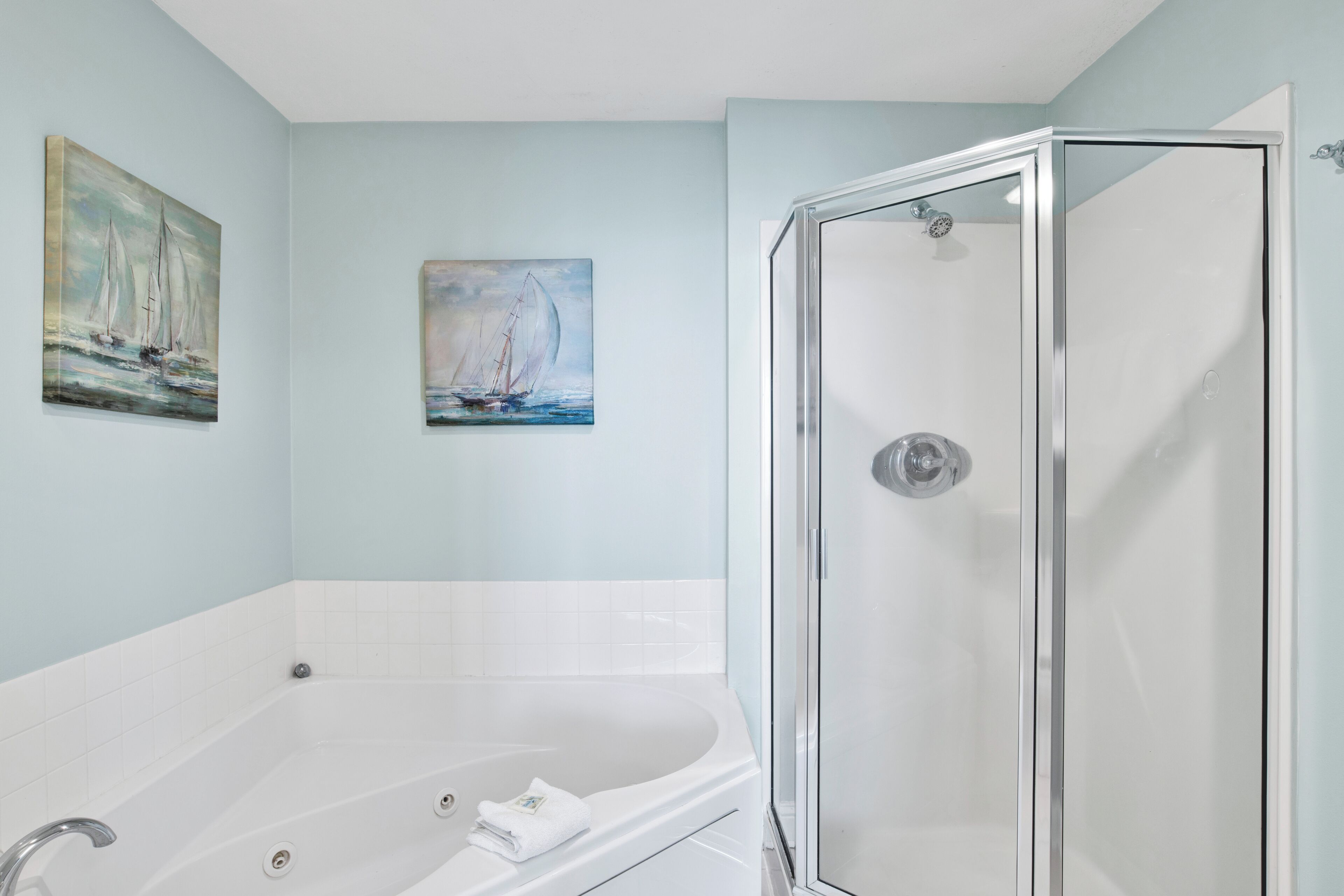 Une salle de bain avec une baignoire, une cabine de douche en verre et deux tableaux accrochés au mur.