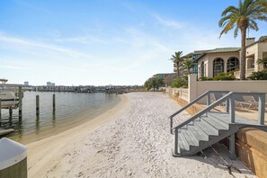 A beach with a wooden staircase leading to a building, a dock, and palm trees. - Lighthouse on the Bay 2310 by Liquid Life (Orange Beach)