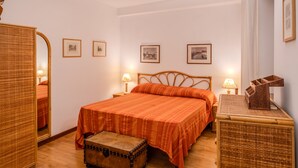 A bedroom with a wooden bed, two bedside tables with lamps, a wooden chest, and framed pictures on the wall. - Navona Romantic House (Roma)