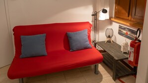 A red sofa with two blue cushions, a small table with a lamp, a fire extinguisher, and a painting on the wall. - Navona Romantic House (Roma)