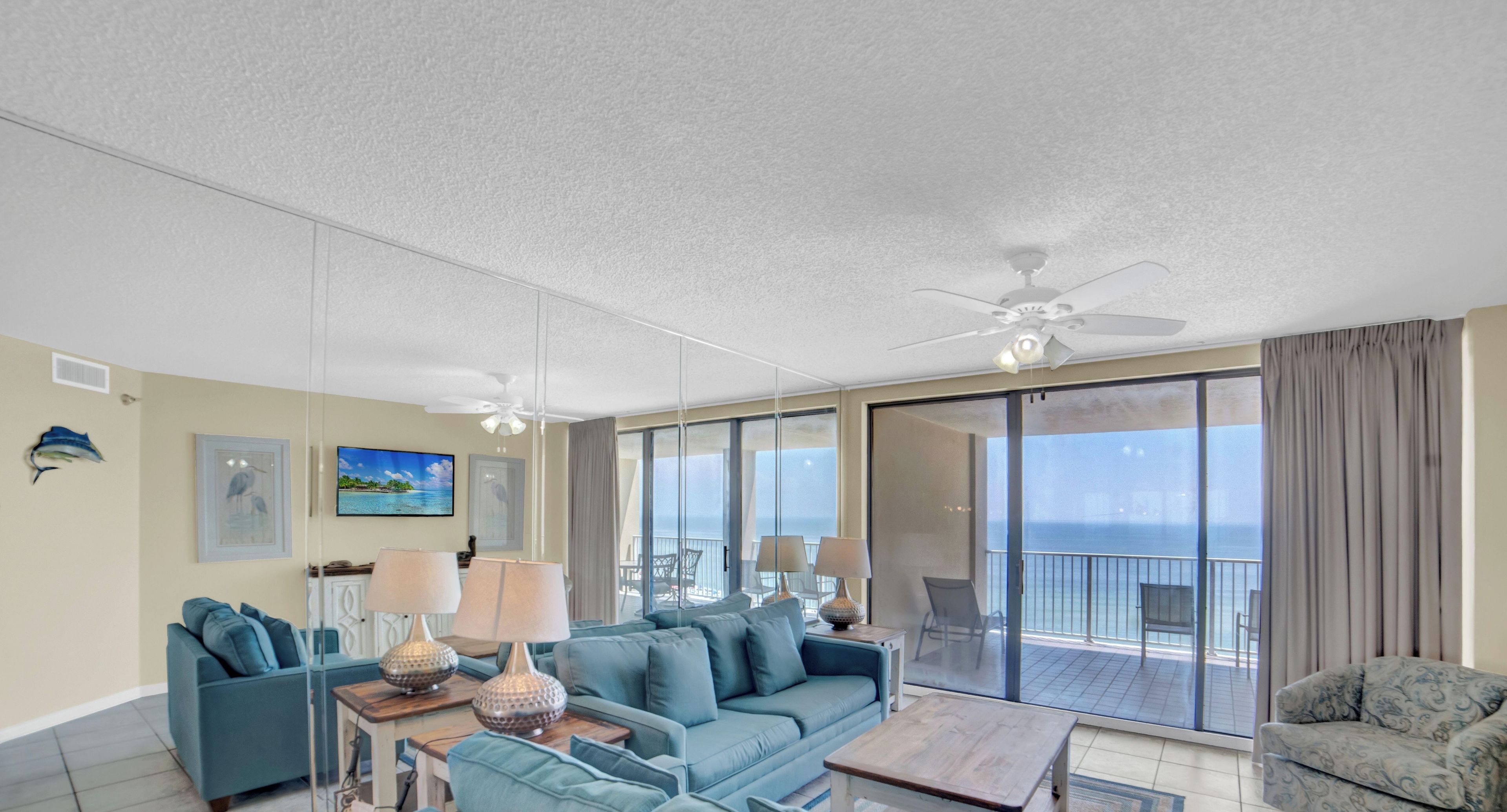 A spacious living room with a large sofa, a coffee table, and a balcony with a view of the sea.