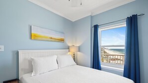 A bedroom with a bed, a nightstand, a lamp, a painting, and a window with curtains. - Tradewinds 1207 by Liquid Life (Orange Beach)