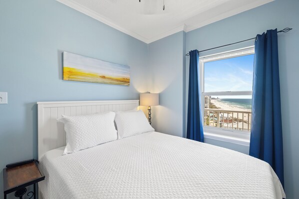 A bedroom with a bed, a nightstand, a lamp, a painting, and a window with curtains.