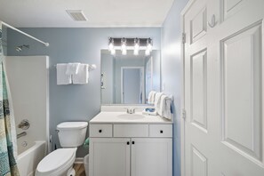 Une salle de bain avec un lavabo blanc, des toilettes, une baignoire et un rideau de douche.
