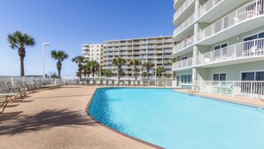 A swimming pool with sun loungers and palm trees, surrounded by a multi-story hotel with balconies. - Tradewinds 1207 by Liquid Life (Orange Beach)