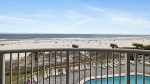 Blick auf einen Strand vom Balkon mit Pool, Liegestühlen und einer Sandstrandanlage.