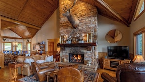 A cozy living room with a stone fireplace, leather furniture, and a mounted deer head. - The Boulders (Boone)
