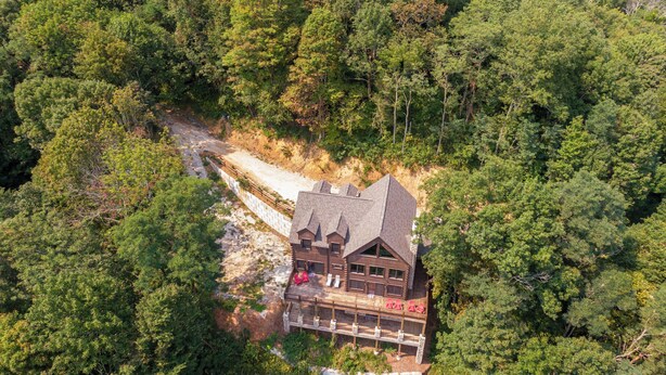 A log cabin with a balcony and a dirt path leading to it, surrounded by dense forest. - Cranberry View Lodge (Newland)
