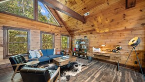 A cozy log cabin interior with a loft bed, a sofa, a coffee table, and a bookshelf. - Cranberry View Lodge (Newland)