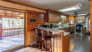 A spacious kitchen with wooden cabinetry, a bar area with stools, and a large window overlooking a deck. - Eagles Rest (Fleetwood)