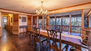 A spacious dining room with a large wooden table and ornate chairs, a chandelier, and large windows offering a view of the outdoors. - Eagles Rest (Fleetwood)
