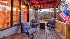 A wooden deck with outdoor seating, a flag, and a view of the mountains. - Banner Bear (Banner Elk)