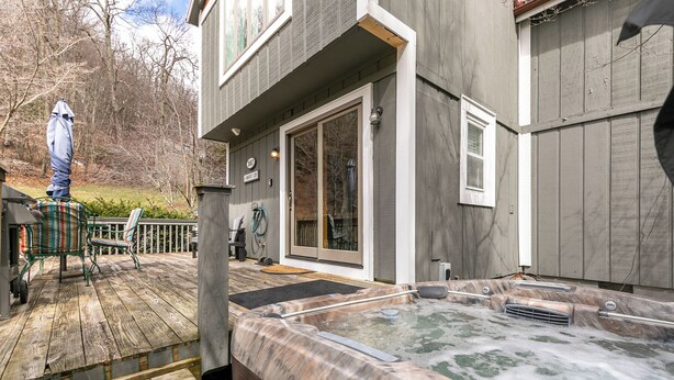 A wooden deck with a hot tub, a covered patio area, and a house with a large sliding glass door. - A Parkway Cabin (Boone)