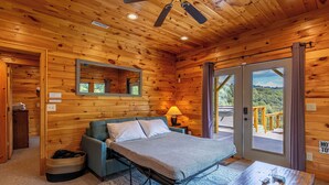 Ein Zimmer in einer Holzhütte mit einem Bett, einem kleinen Tisch, einer Lampe und einem Fenster mit Blick.
