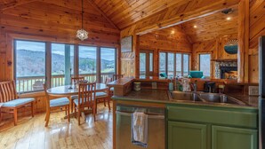 Ein Holzblockhaus-Interieur mit Essbereich, Küche und großen Fenstern, die einen Blick ins Freie bieten.