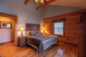 A wooden cabin bedroom with a bed, two bedside tables with lamps, a window with blinds, and a wooden headboard. - A Moon River View (Boone)