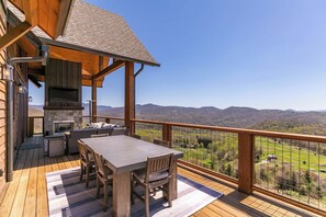 Une terrasse en bois avec un foyer en pierre, des sièges d’extérieur et une vue panoramique sur les montagnes.