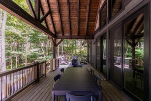 A covered deck with a table and chairs, surrounded by glass doors and windows, overlooking a forested area. - BaseCamp at Eagles Nest (Banner Elk)