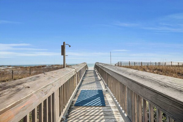 A wooden boardwalk leading to a beach with a clear sky.