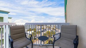 Ein Balkon mit zwei Stühlen und einem kleinen Tisch, mit Blick auf einen Parkplatz und Gebäude.
