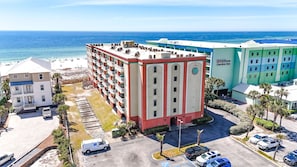 A hotel with multiple floors, a parking lot, and a beach view.