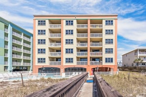 A multi-story hotel with balconies, a pool, and a wooden boardwalk leading to the entrance.