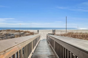 A wooden boardwalk leading to a beach with a clear sky.