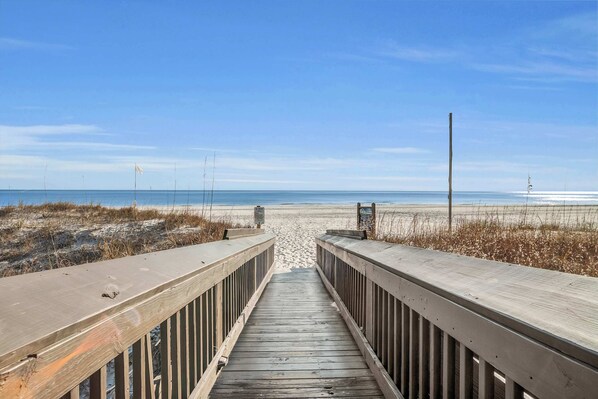 A wooden boardwalk leading to a beach with a clear sky.