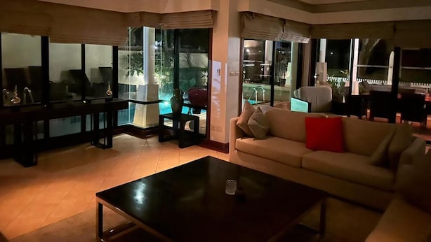 Ein modernes Wohnzimmer mit einem großen, schwarzen Couchtisch, einem beige gefärbten Sofa mit roten Kissen und einem Fernseher auf einem schwarzen Lowboard.