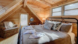 Een knus slaapkamer op zolder met een bed, een bloemenbank en een raam met uitzicht op een bos.