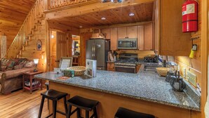 A cozy cabin-style kitchen with wooden walls, a granite countertop, and modern appliances. - Bearadise at Blue Ridge (West Jefferson)