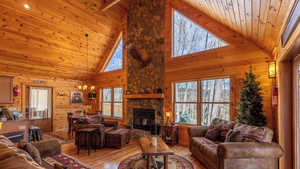 A log cabin interior with a stone fireplace, wooden furniture, and large windows. - Bearadise at Blue Ridge (West Jefferson)