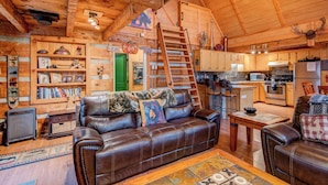 A cozy cabin interior with a leather sofa, wooden walls, a kitchen area, and a ladder leading to a loft. - Bridgepoint Cabin (Vilas)