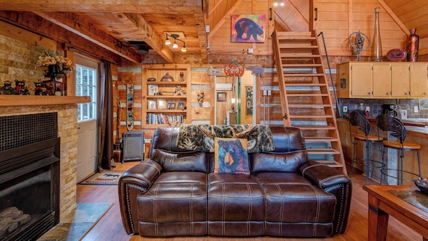 A cozy cabin interior with a fireplace, leather sofa, wooden shelves, and a staircase leading to an upper level. - Bridgepoint Cabin (Vilas)