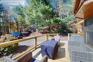 A deck with outdoor furniture, a covered table, and a view of a forested area. - Napping Bear Cabin (Boone)
