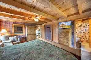A cozy room with a bed, a dresser, a television, and a plaid-patterned wall. - Napping Bear Cabin (Boone)