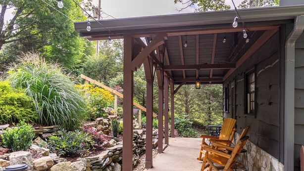 A wooden porch with a covered seating area, stone walls, and a variety of plants. - Sky Laurel Cottage (Blowing Rock)