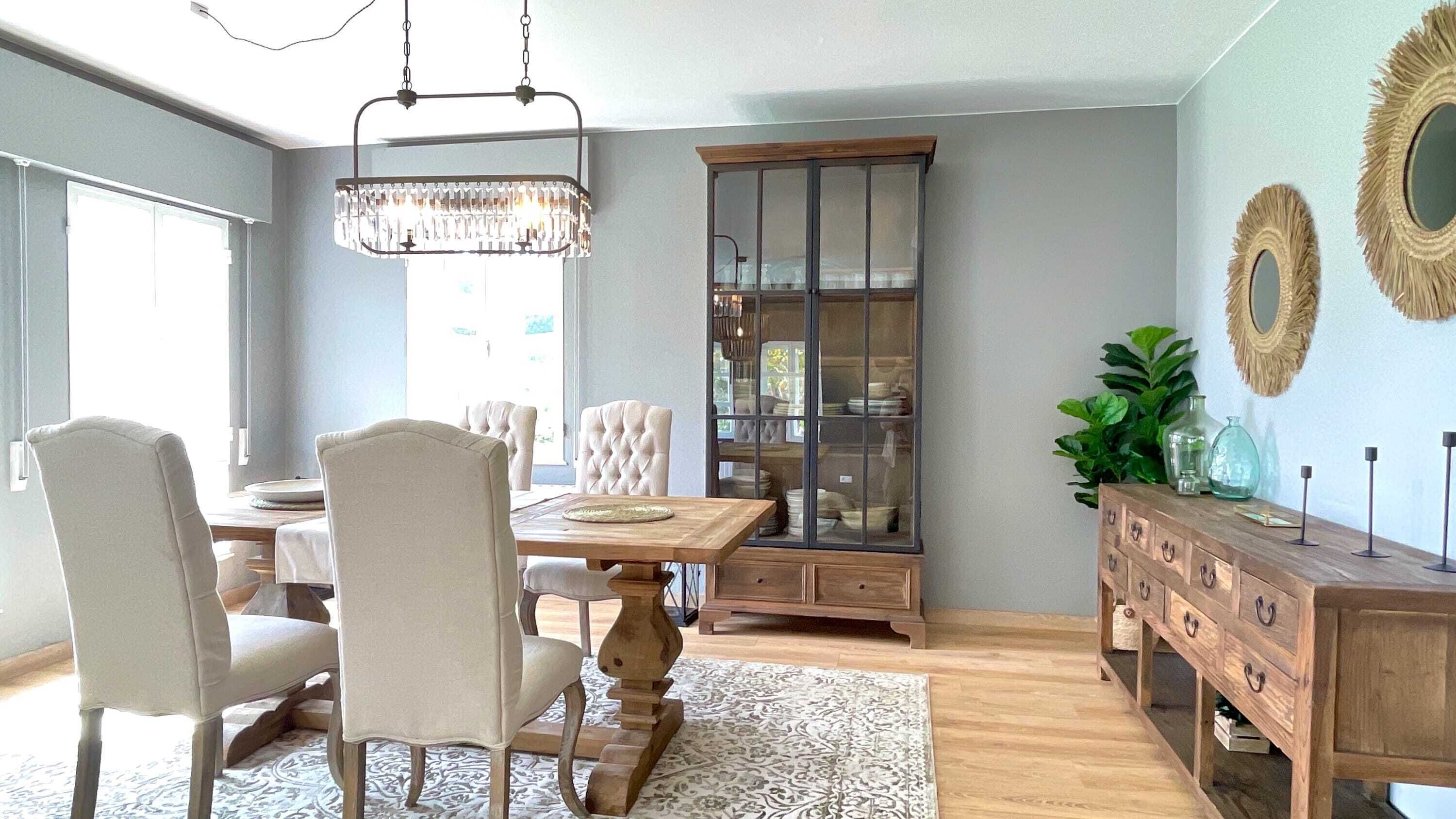 A dining area with a wooden table and chairs, a chandelier, a glass-fronted cabinet, and a wooden dresser with decorative mirrors.