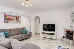 A modern living room with a grey sofa, a flat-screen TV, a fireplace, and a colorful abstract painting on the wall. - Villa Auspana (Mijas)