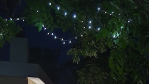 Un espacio al aire libre techado con luces colgantes, un banco y un pequeño edificio iluminado.