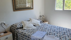 Un dormitorio con cama, mesita de noche, lámpara y ventana.
