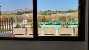 Una habitación con un amplio ventanal que da a una zona de piscina con sillas de descanso y un paisaje montañoso.